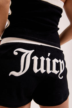 Displays a model wearing the Black Appliqué 'Juicy' branded  Terry booty shorts featuring the juicy branding 