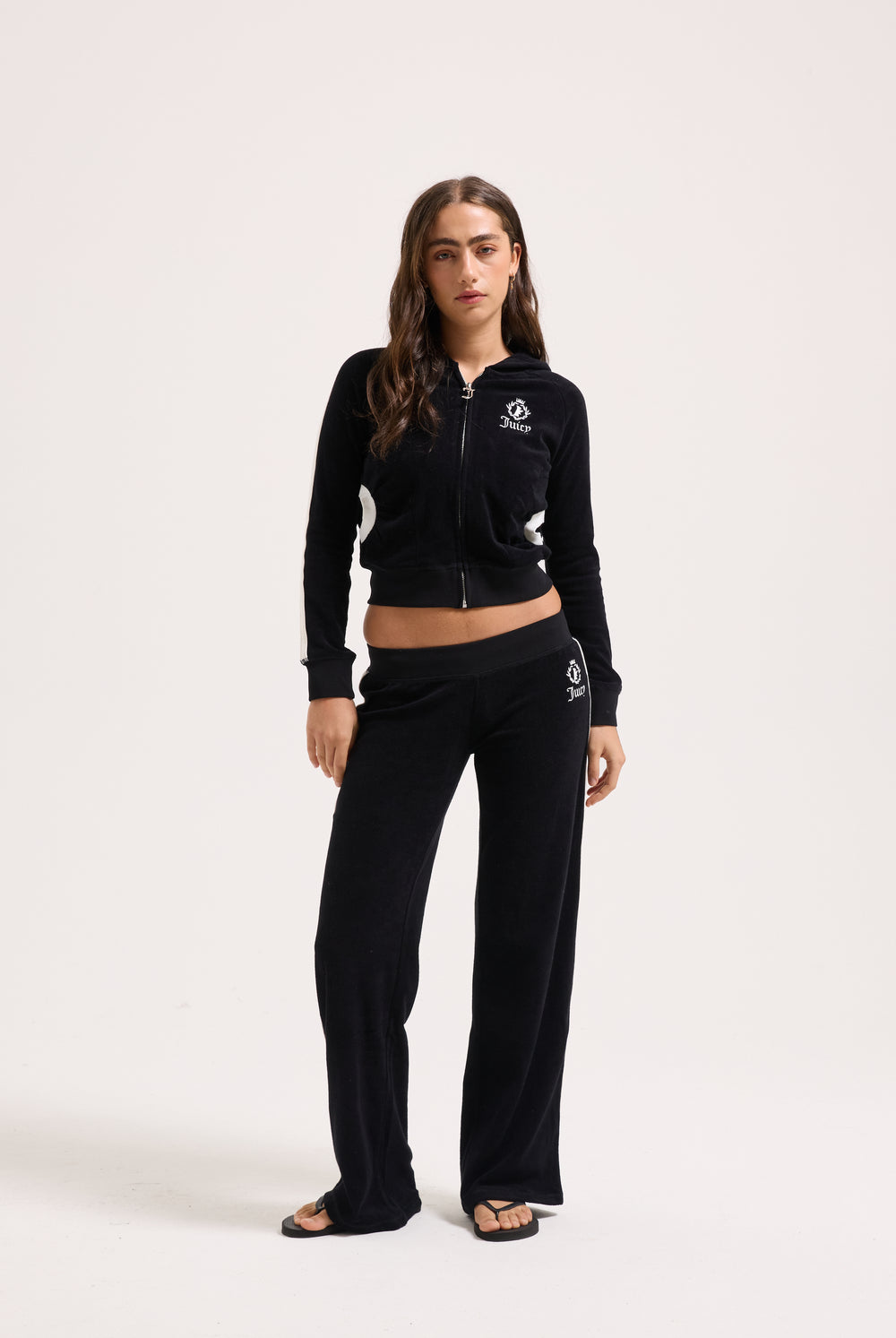 Displays a model wearing the Black appliqué 'Juicy' branded Terry ultra low straight track pants 