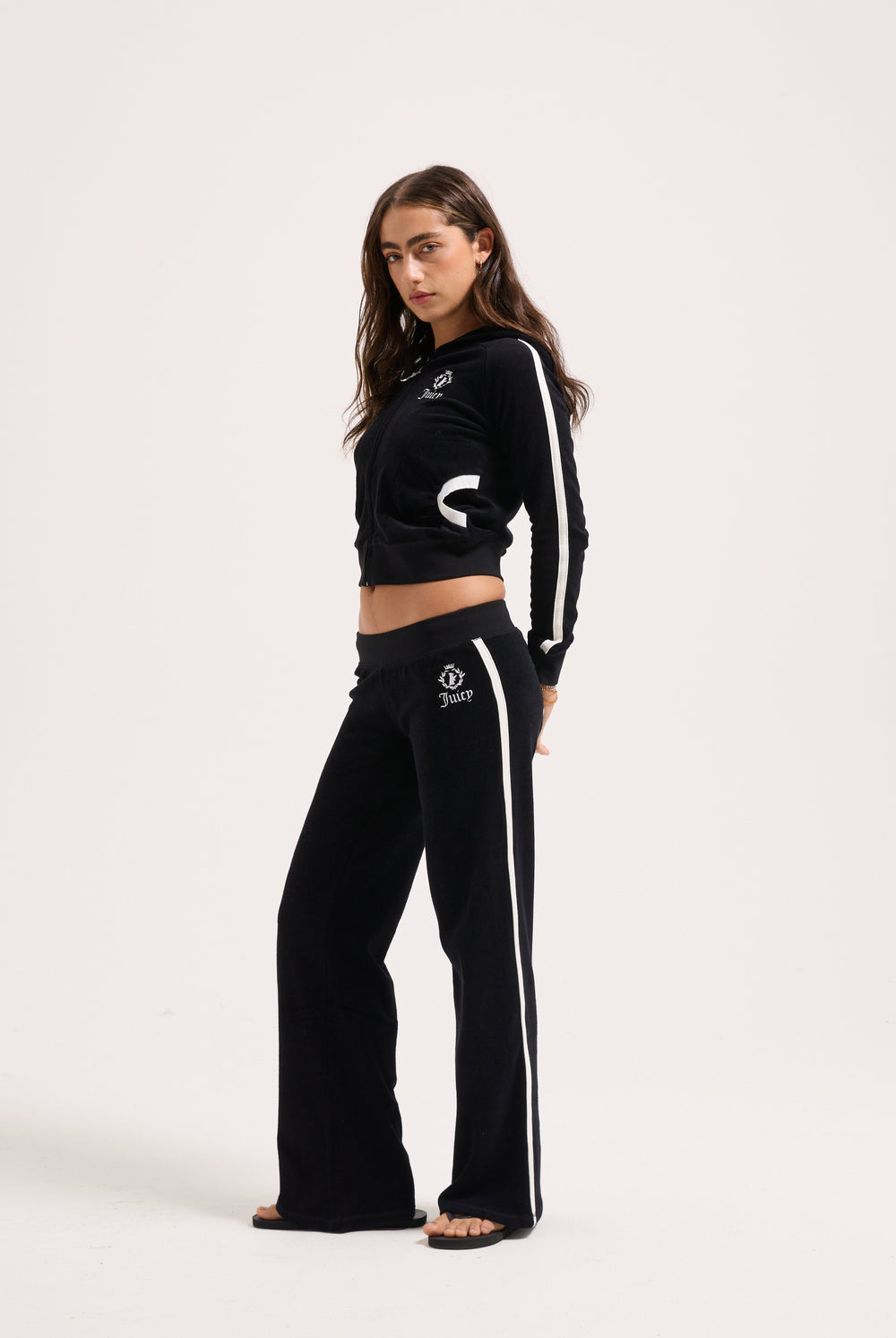 Displays a model wearing the Black appliqué 'Juicy' branded Terry ultra low straight track pants 