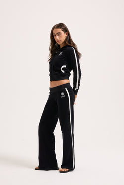 Displays a model wearing the Black appliqué 'Juicy' branded Terry ultra low straight track pants 