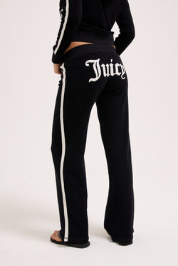 Displays a model wearing the Black appliqué 'Juicy' branded Terry ultra low straight track pants 