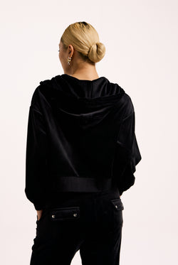Displays a model wearing the Black 'Juicy' branded crop oversized classic velour hoodie 