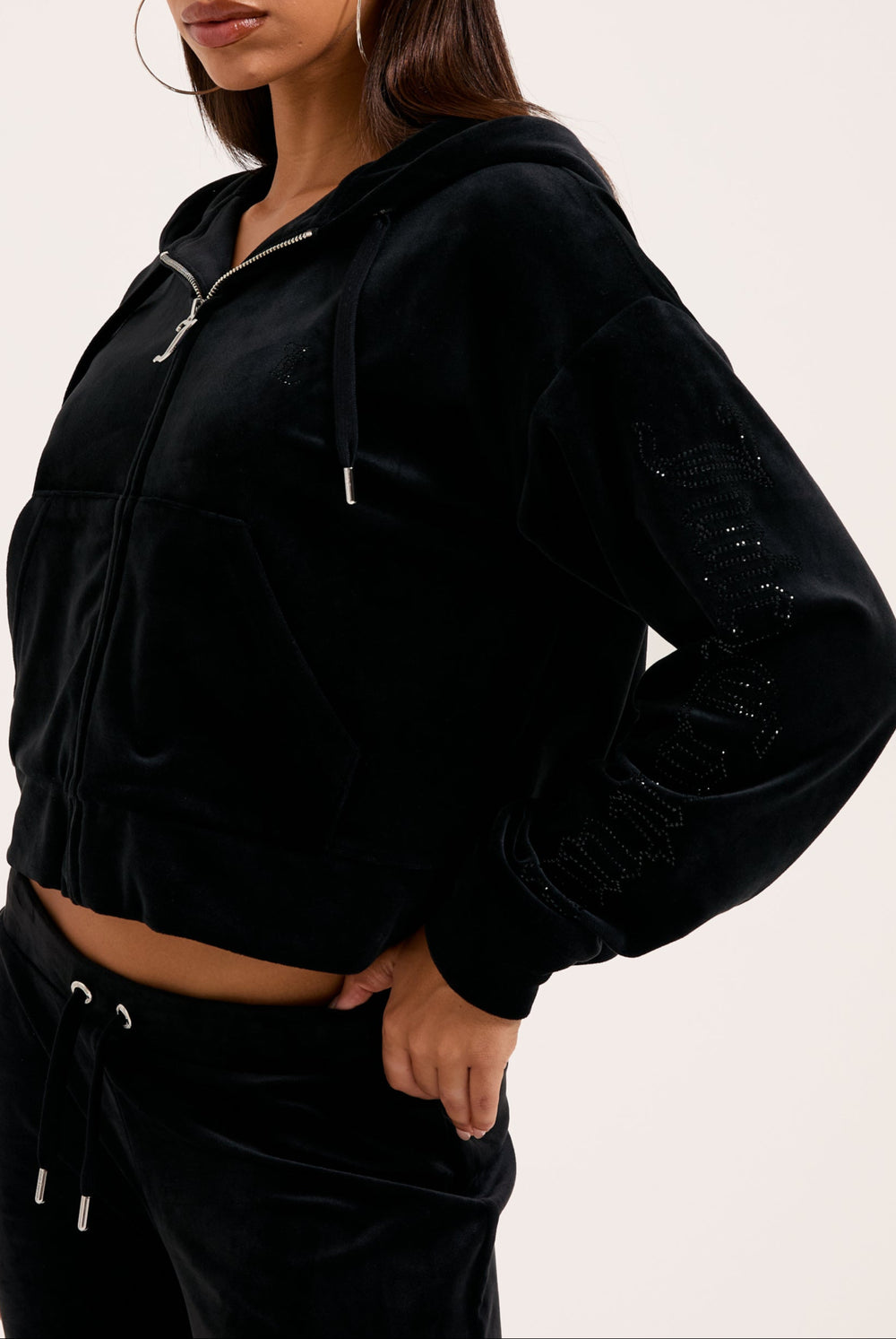 Displays a model wearing the Black 'Juicy' branded outline diamanté oversized cropped hoodie 