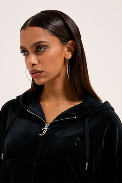 Displays a model wearing the Black 'Juicy' branded outline diamanté oversized cropped hoodie 