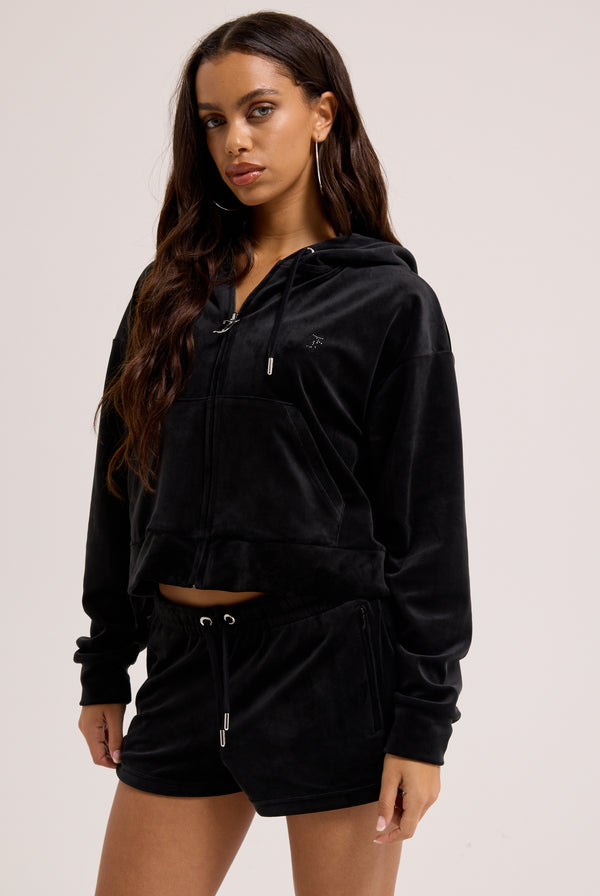 Displays a model wearing the Black 'Juicy' branded velour outline diamanté track shorts 