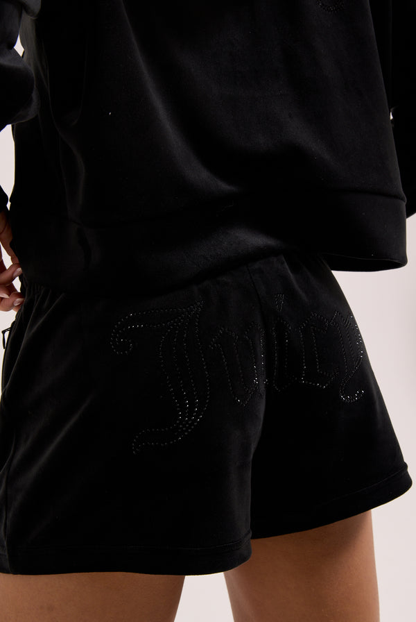 Displays a model wearing the Black 'Juicy' branded velour outline diamanté track shorts 