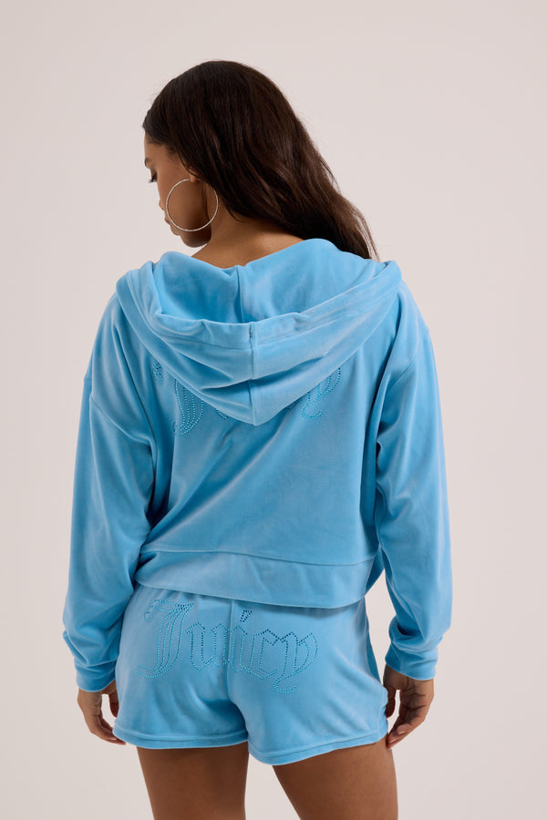 Displays a model wearing the Sky Blue 'juicy' branded Velour outline diamanté track shorts 
