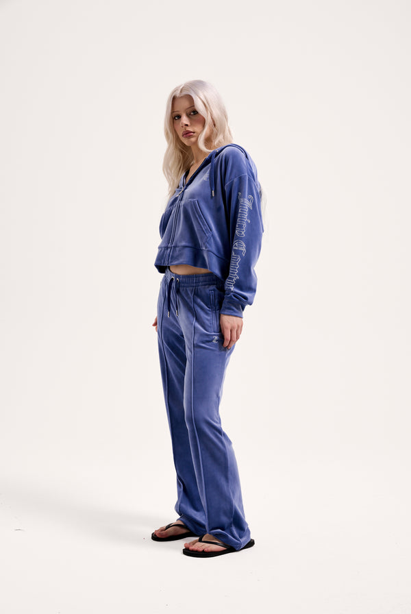 Displays a model wearing the grey blue 'Juicy' branded velour outline diamanté tracksuit bottom