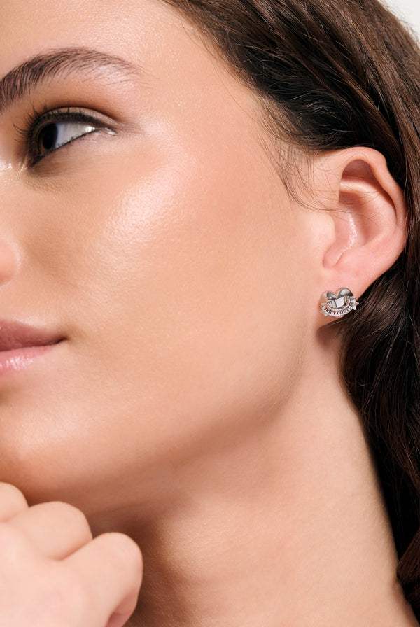 Displays a model wearing the Silver Tone 'Juicy' icon heart stud earrings 