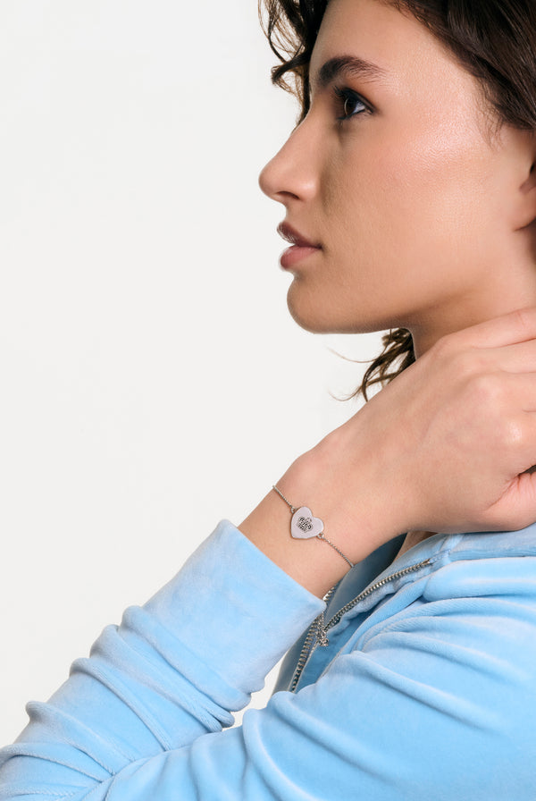 Displays a model wearing the silver tone 'Juicy' branded reversible heart adjustable bracelet 
