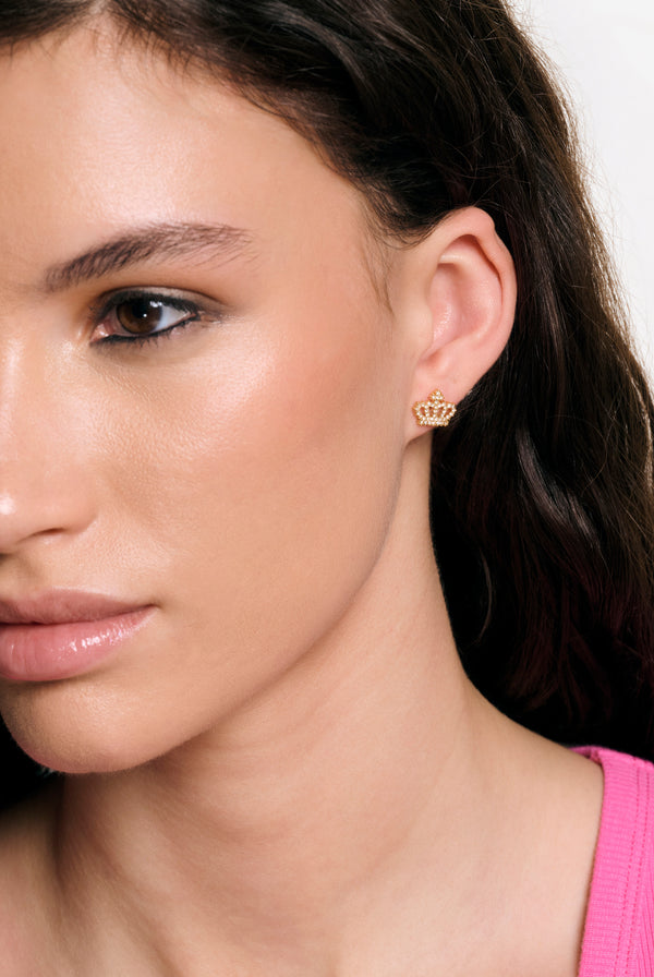Displays a model wearing the Gold Tone 'Juicy' branded crystal motif crown stud earrings 