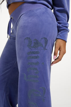 Displays a model wearing the Greyblue 'Juicy' branded Old Gothic Diamante OG Straight Leg Trackpant featuring the details on the juicy branding 