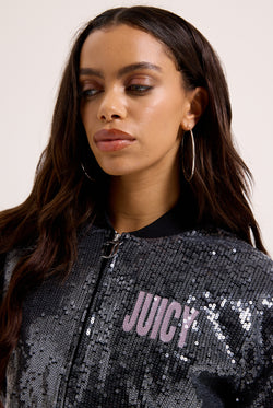 Displays a model wearing the 'juicy' branded choose juicy sequin cropped bomber featuring the juicy branding 