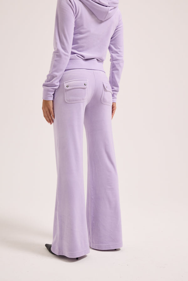 Displays a model wearing the pastel lilac 'juicy' branded low rise flare classic velour track pant 