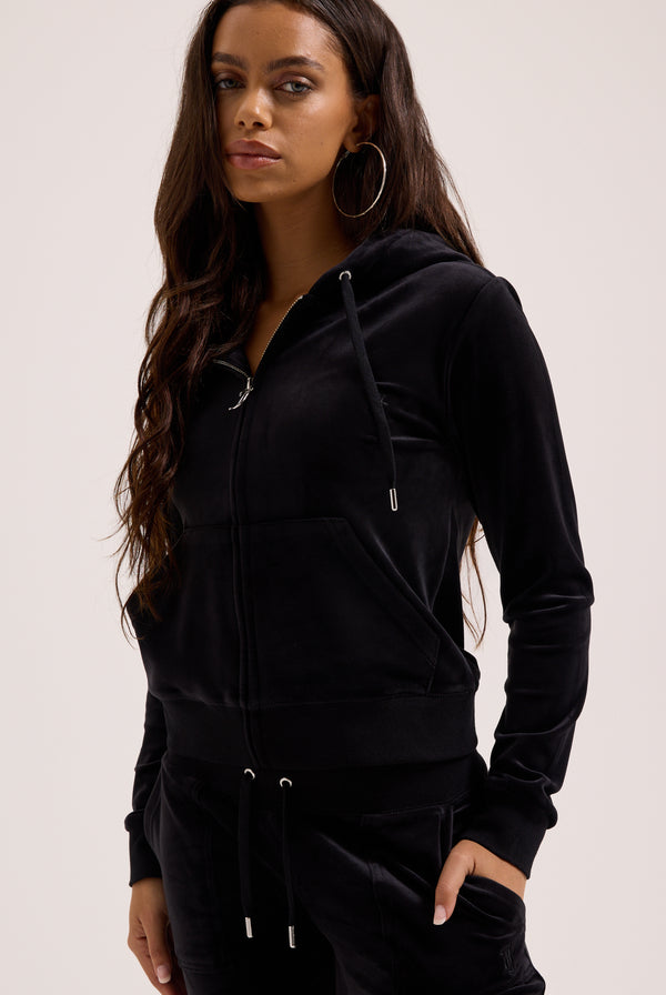 Woman wearing a black hoodie and pants on a light pink background
