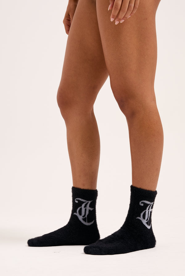 Displays a model wearing the Black seasonal 'Juicy' branded fluffy sock included in the 2 pack 