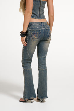 Displays a model wearing the Mid Wash 'Juicy' branded Sand Stud Moto Bootcut Jeans
