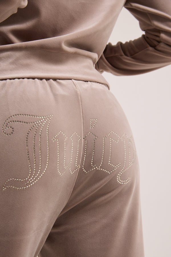Displays a model wearing the jungle outline 'juicy' branded velour diamanté tracksuit bottom featuring the juicy branding