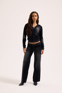 Displays a model wearing the washed black cotton 'Juicy' branded velour og straight low rise pants 
