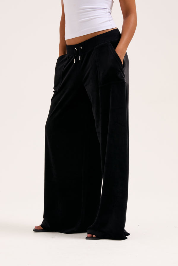 Display a model wearing the Black 'Juicy' branded wide leg classic velour track pant 