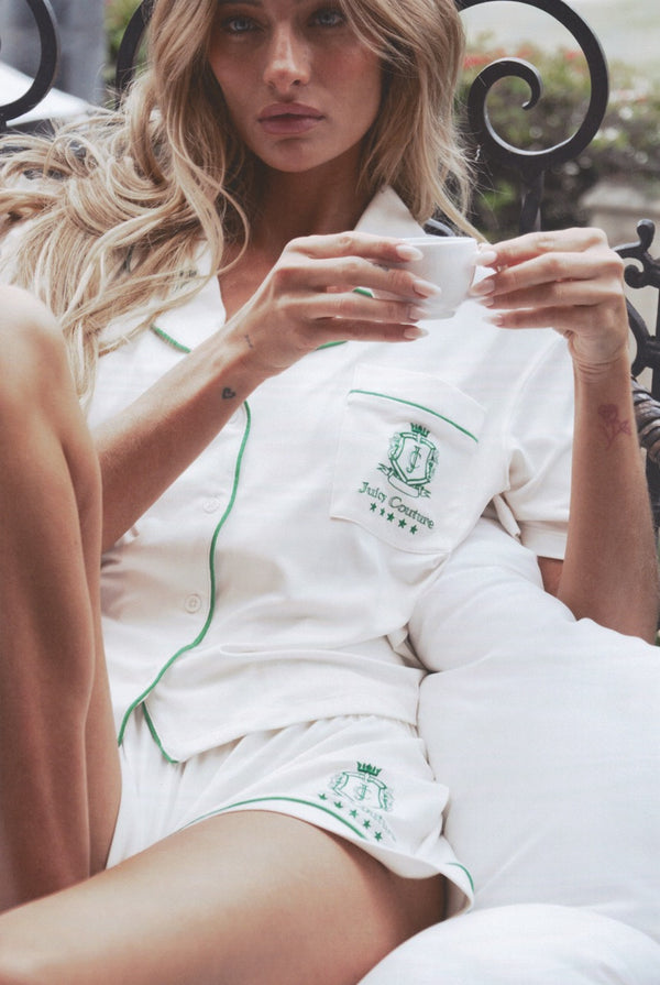 Woman in a white set with green embroidery holding a cup outdoors.